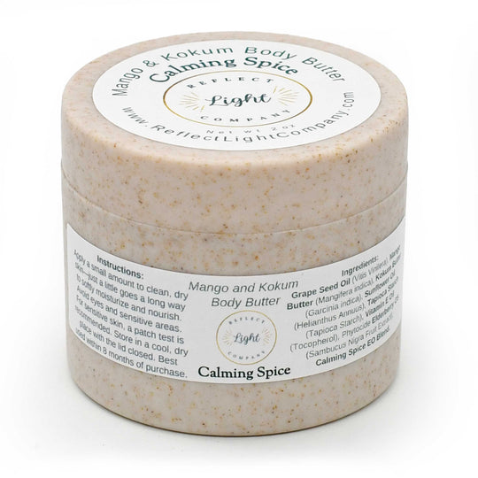 A round jar of Mango and Kokum Body Butter with Calming Spice by Reflect Light Company, featuring a beige speckled texture and white labels.