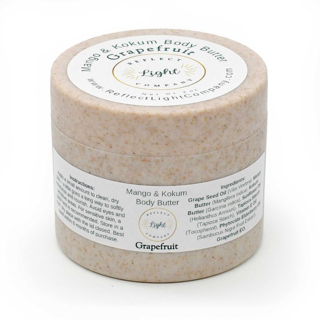 A round jar of Grapefruit Mango & Kokum Body Butter by Reflect Light Company, featuring a speckled beige product inside and white labels with black and gold text.