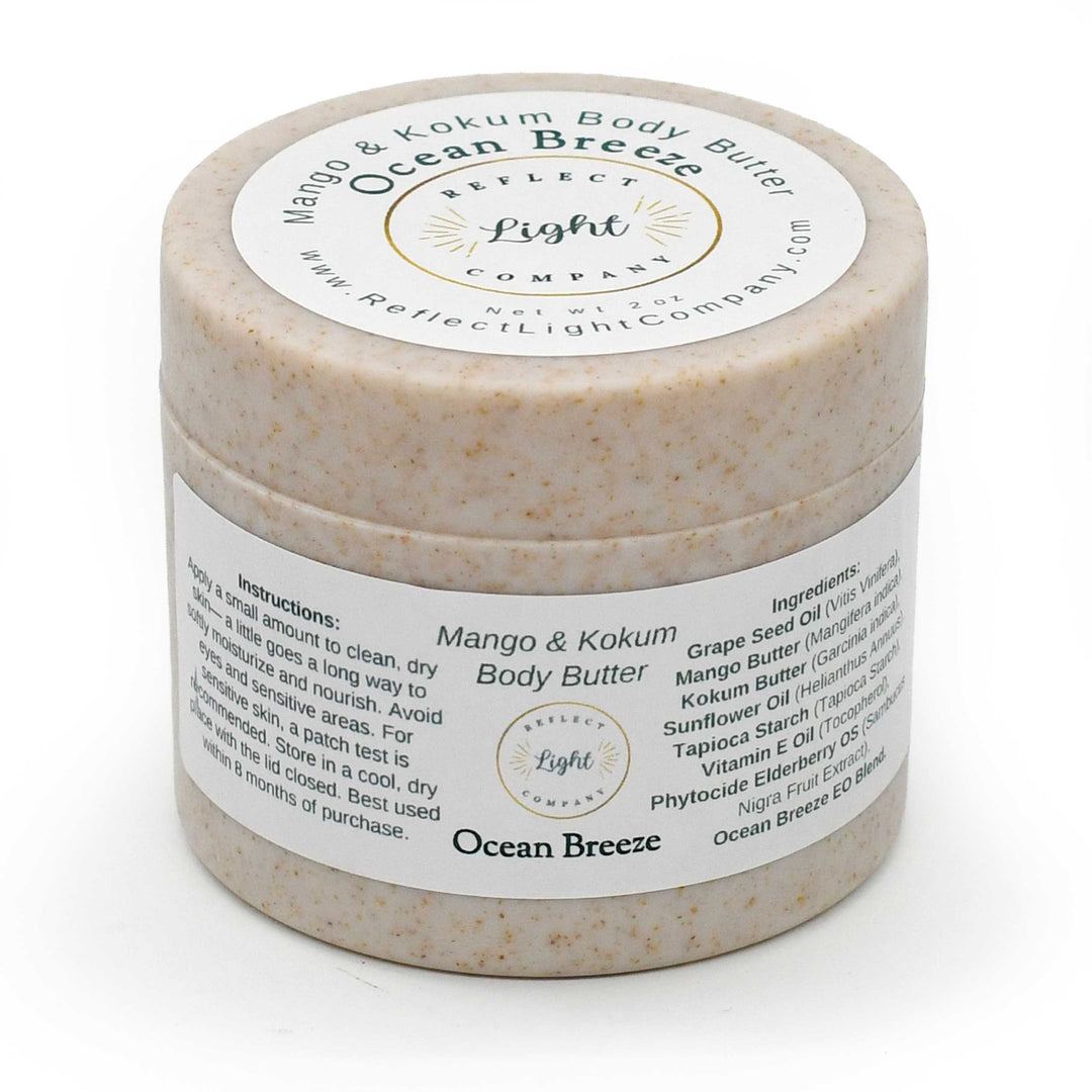 A jar of Reflect Light Company Mango & Kokum Body Butter in the Ocean Breeze scent, showing the textured beige body butter through the clear plastic jar and its white labels.