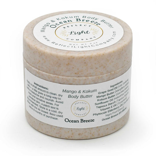 A jar of Reflect Light Company Mango & Kokum Body Butter in the Ocean Breeze scent, showing the textured beige body butter through the clear plastic jar and its white labels.