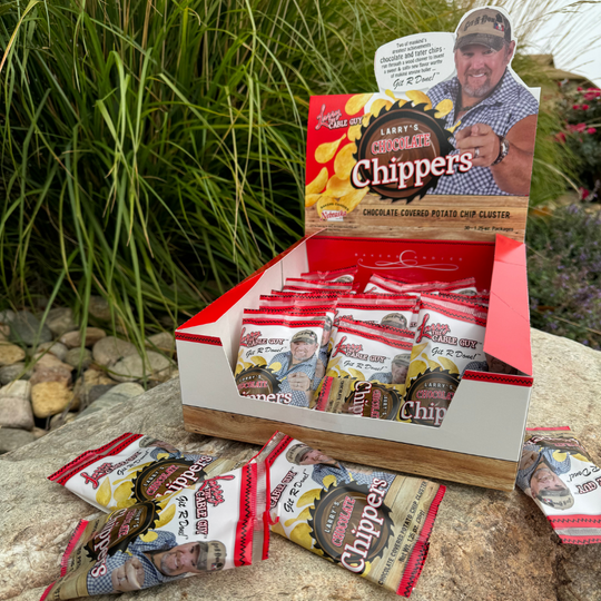 Product box full of Baker's Candies Larry's Chocolate Chippers: Chocolate covered potato chip clusters. Placed on a rock with a grass background.