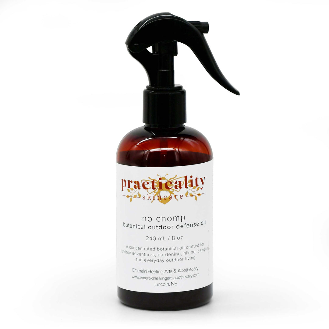 A 240 mL amber glass spray bottle of Practicality Skincare 'No Chomp' botanical outdoor defense oil, featuring a black trigger sprayer and a white label with gold and red text, set against a plain white background.