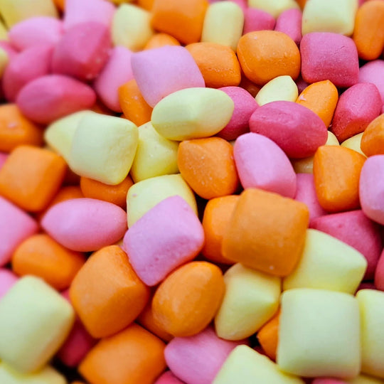 A close-up pile of small, pastel-colored candy pieces in pink, orange, and pale yellow.