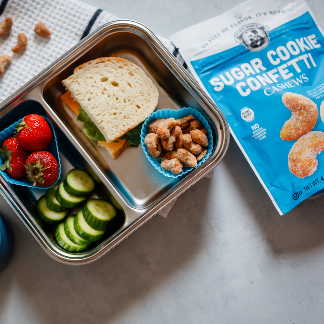 Lunchbox with sandwich, fruits, and vegetables next to packages of Sugar Cookie Confetti cookies.