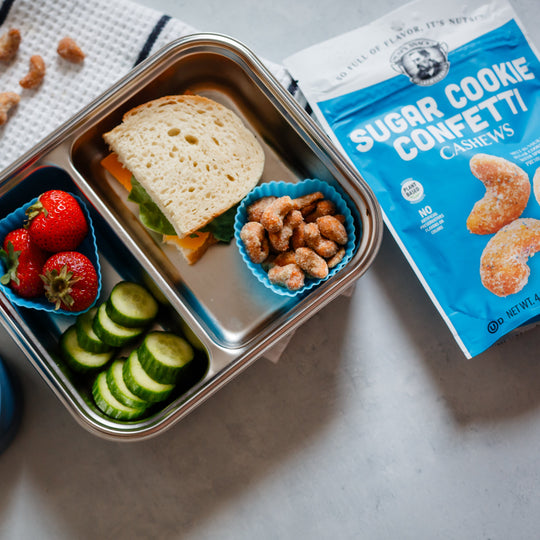 Lunchbox with sandwich, fruits, and vegetables next to packages of Sugar Cookie Confetti cookies.