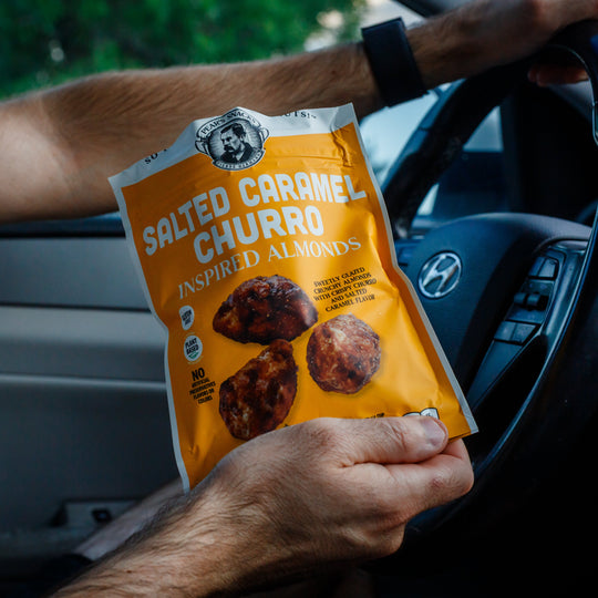 Person holding a package of Salted Caramel Churro inspired almonds inside a car.