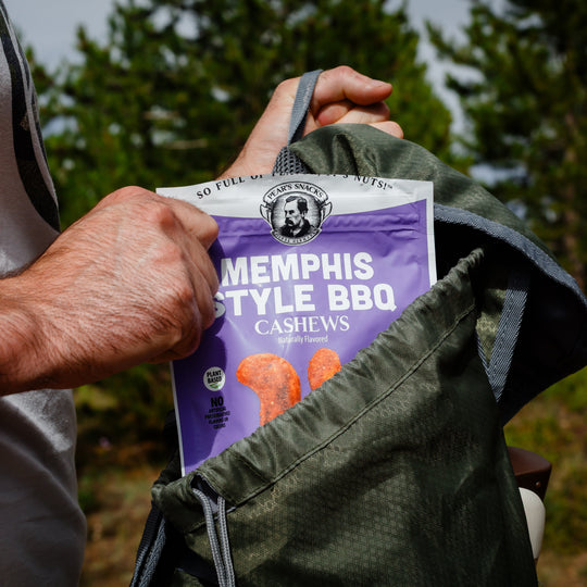 Person holding a bag of Memphis Style BBQ cashews with a natural outdoor background