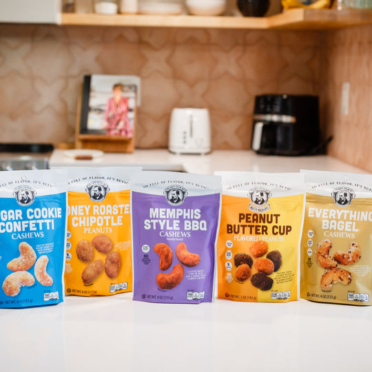 Five packages of different flavored cashews on a kitchen counter.