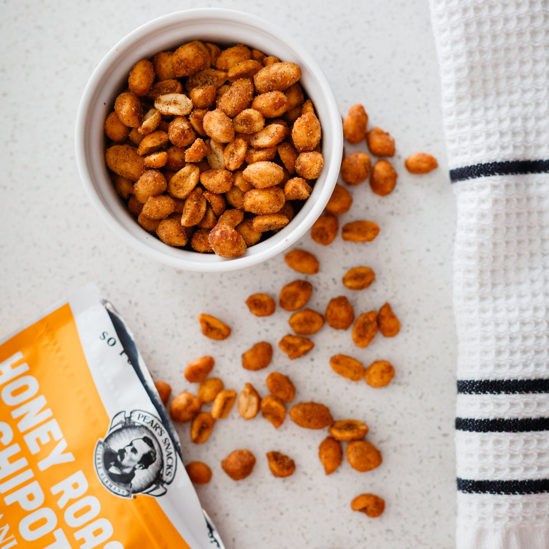 Honey roasted peanuts in a bowl with a packet of Honey Roasted Peanuts on a light surface.