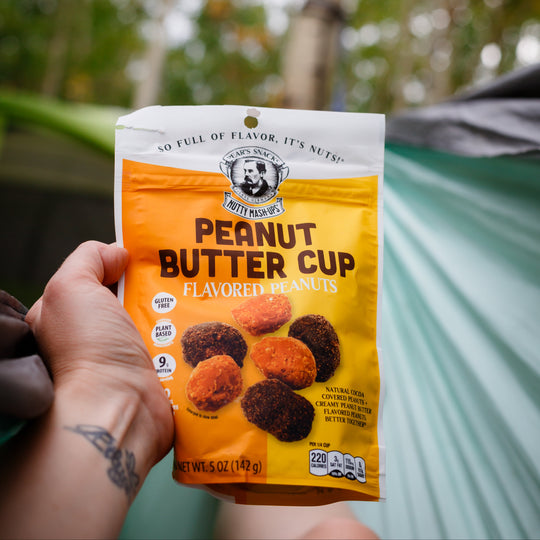 Hand holding a package of Peanut Butter Cup flavored snacks with a forest background