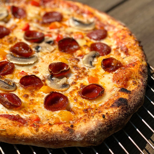 Personal-sized pizza with pepperoni and mushrooms on a grill