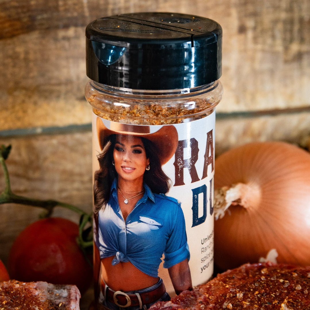Ranch Dust seasoning bottle with a label featuring a person, surrounded by raw meat and vegetables on a wooden surface.