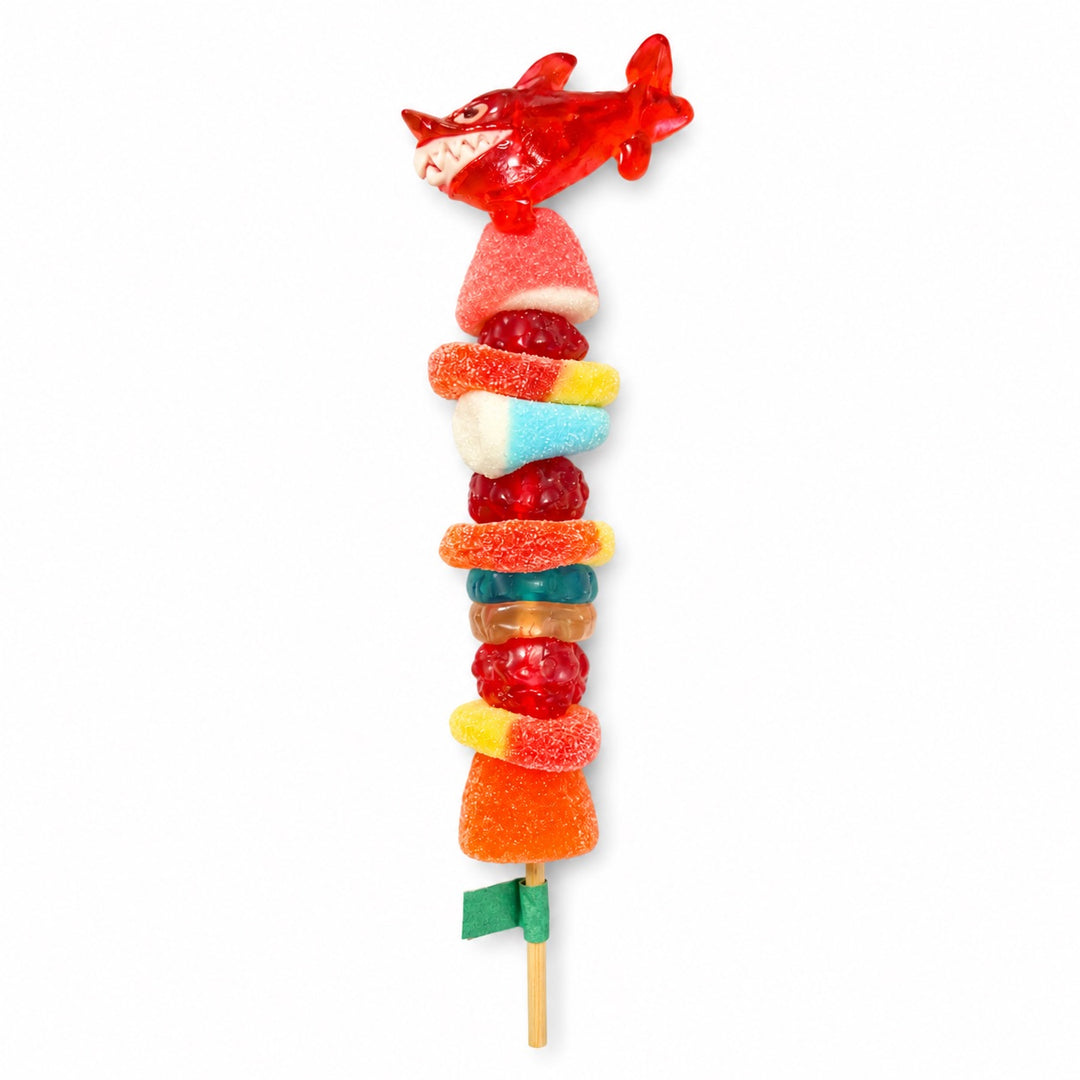 Red shark candy kabob topped with a red shark gummy and stacked with assorted gummy candies on a wooden skewer, isolated on a white background.