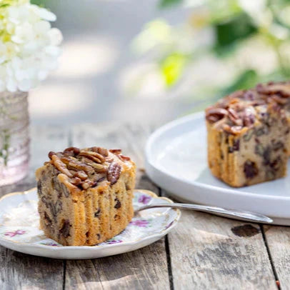 Pecan cake on a wooden table with flowers in the background.