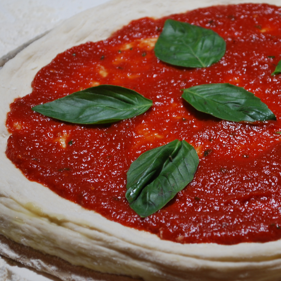 Uncooked pizza with tomato sauce and basil leaves on a white background