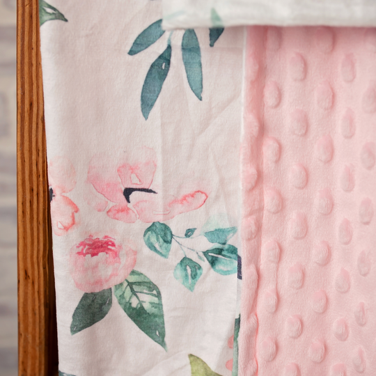 Two baby blankets, one with floral pattern and the other pink minky, on a wooden surface.