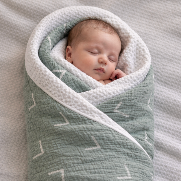 Newborn baby wrapped in a textured green and white blanket on a soft surface