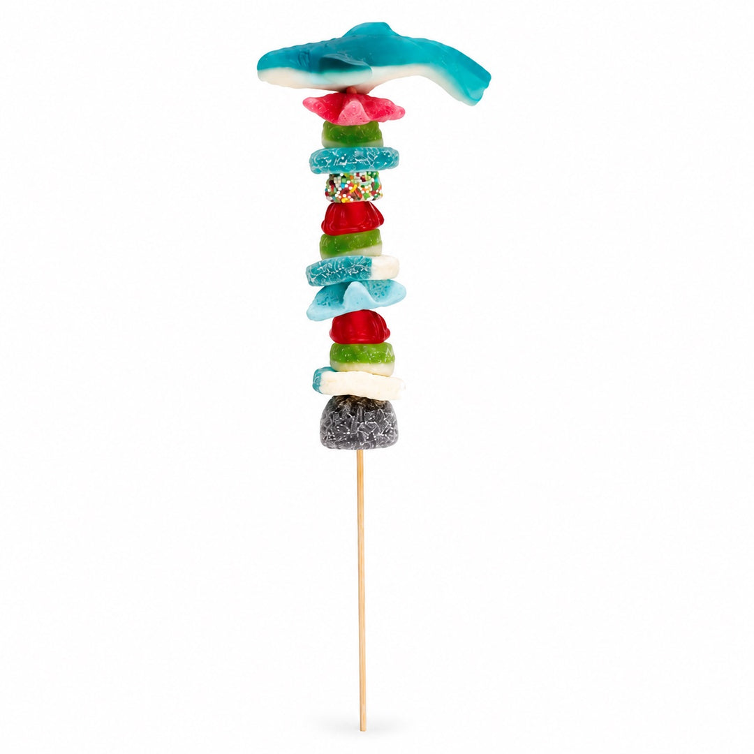 Shark candy kabob featuring a blue shark gummy and colorful gummy candy assortment on a wooden skewer, isolated on a white background.