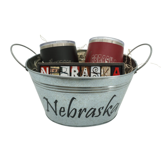 Metal bucket with 'Nebraska' text containing tumblers and a magazine on a white background