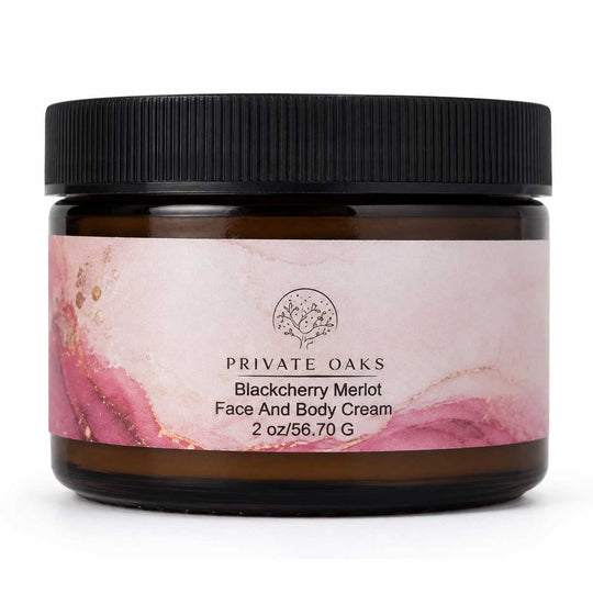 A jar of Private Oaks Blackberry Merlot Face And Body Cream, featuring a dark amber glass jar, a black ribbed lid, and a pink watercolor-patterned label on a white background.