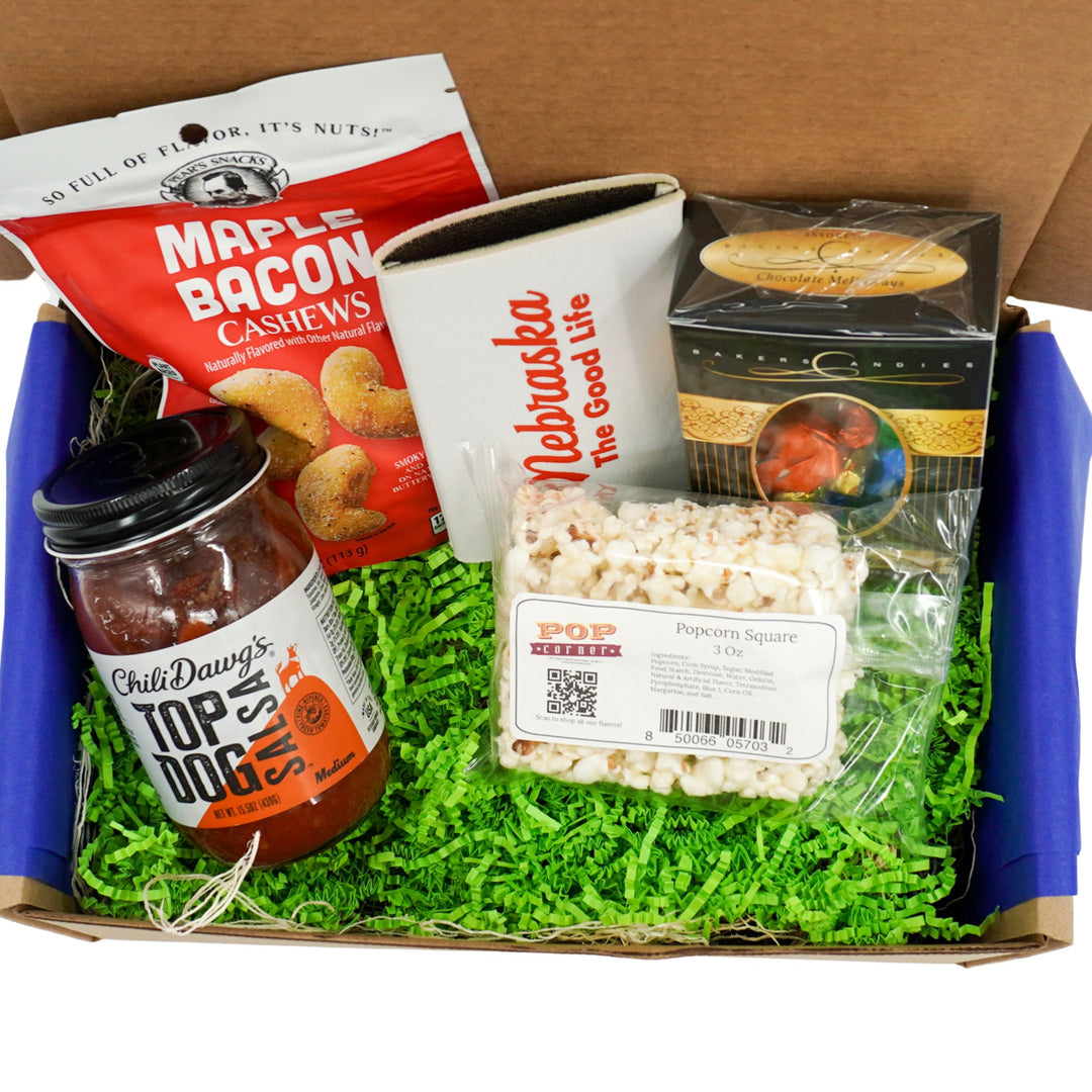 Assorted snacks and treats in a box including cashews, popcorn, and salsa