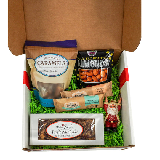 Gift box with caramels, almonds, turtle nut cake, and a Santa Claus figurine on a white background