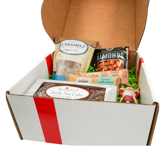 Gift box with assorted snacks and treats including caramels, almonds, and a turtle nut cake on a white background.