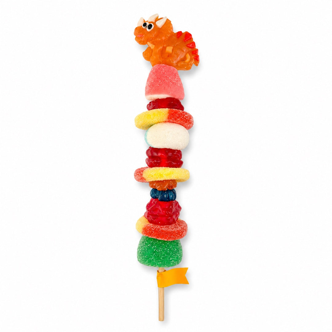 Triceratops candy kabob topped with a orange triceratops gummy and stacked with assorted gummy candies on a wooden skewer, isolated on a white background.