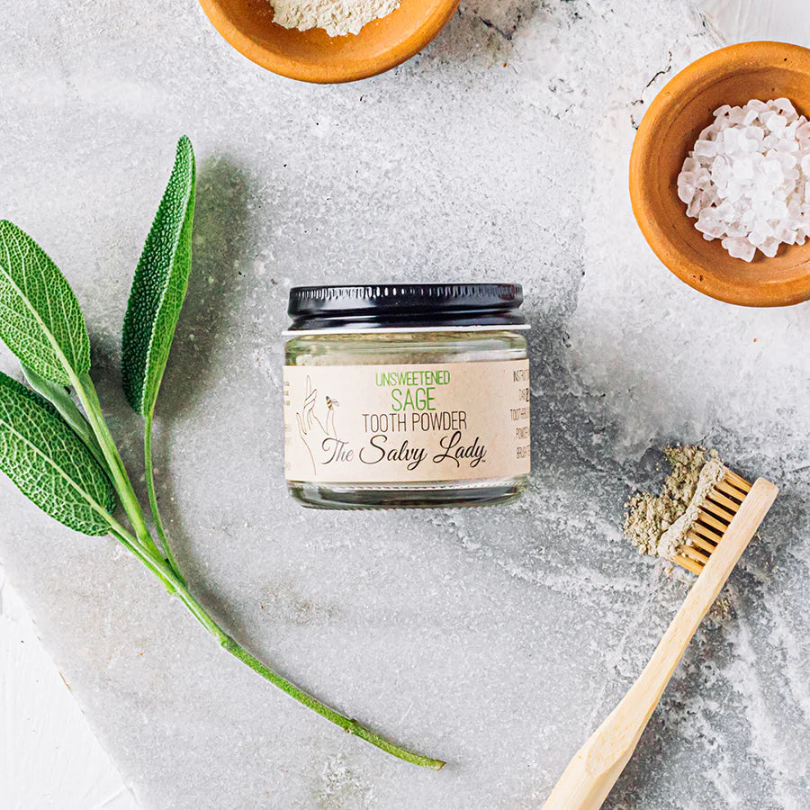 Jar of tooth powder with sage leaves and a wooden brush on a textured surface
