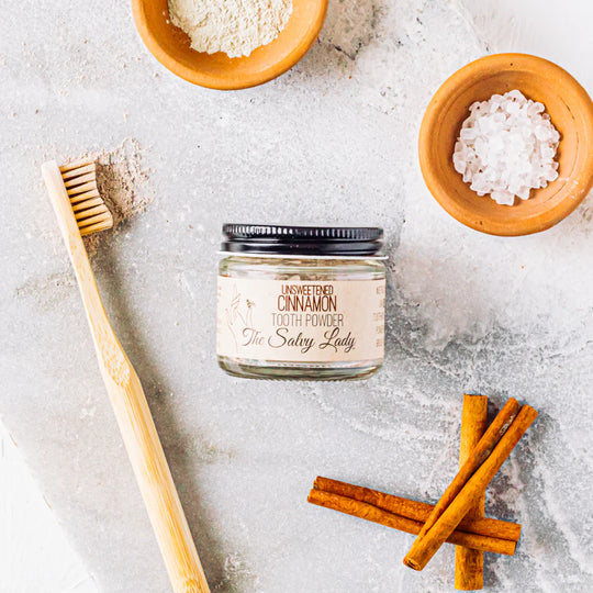 Jar of cinnamon tooth powder with a bamboo toothbrush and cinnamon sticks on a light surface.