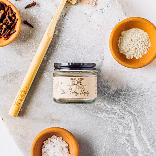 Jar of tooth powder with wooden spoon and bowls on a textured surface