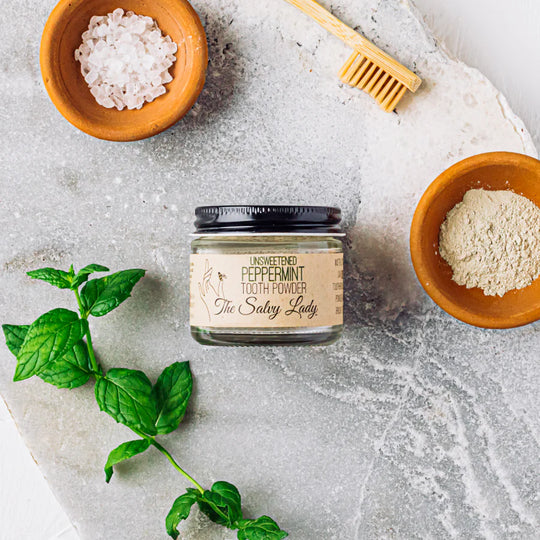 Jar of tooth powder with ingredients on a stone surface
