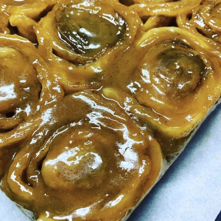 Close-up of a tray of cinnamon rolls with a glossy glaze on a blue surface.