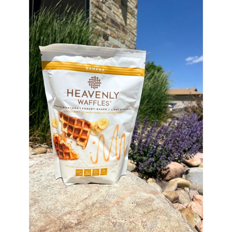 A 13.5 oz. Bag Of Banana Heavenly Waffles Pictured Outside On A Rock WIth A Floral Background 