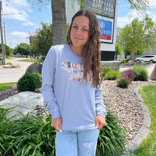 Girl wearing long sleeve gray nebraska license plate shirt.