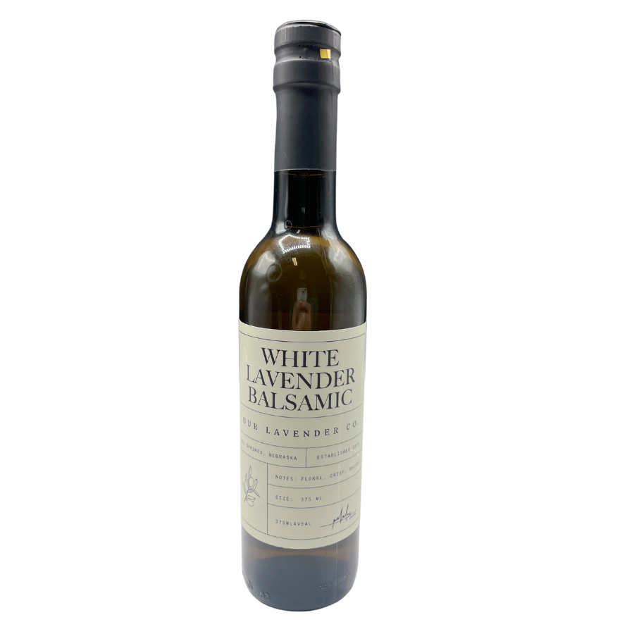 A glass bottle of White Lavender Balsamic Vinegar with a black cap and a label that includes the product name and the brand, Our Lavender Co.