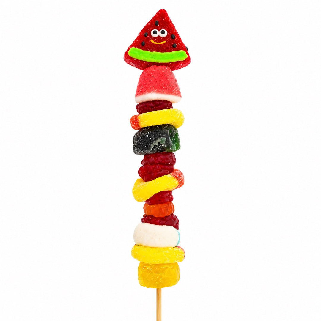 Watermelon candy kabob topped with a smiling watermelon gummy and stacked with assorted gummy candies on a wooden skewer, isolated on a white background.