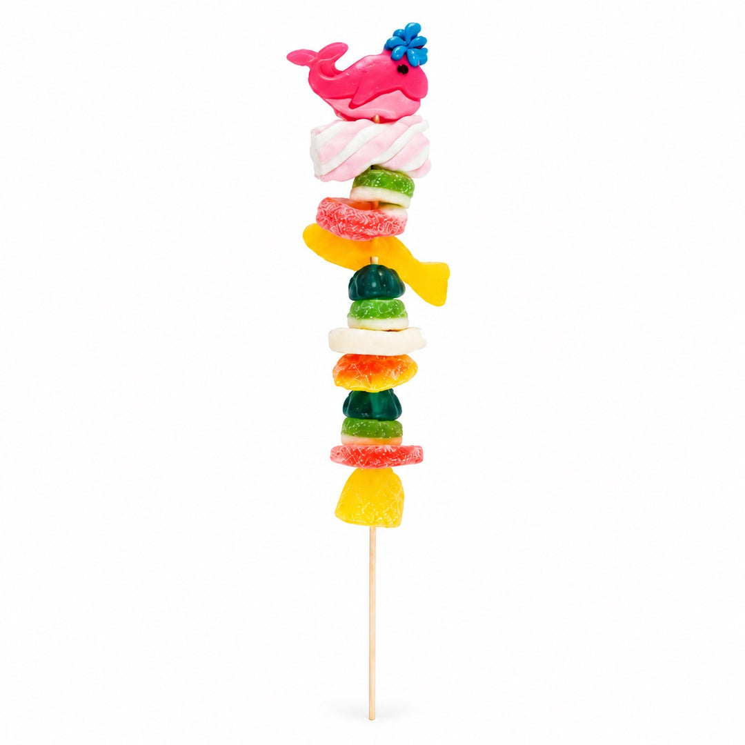 Whale candy kabob topped with a pink whale gummy and layered with assorted fruity gummy candies on a wooden skewer, isolated on a white background.