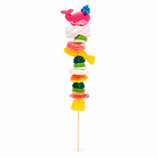 Whale candy kabob topped with a pink whale gummy and layered with assorted fruity gummy candies on a wooden skewer, isolated on a white background.