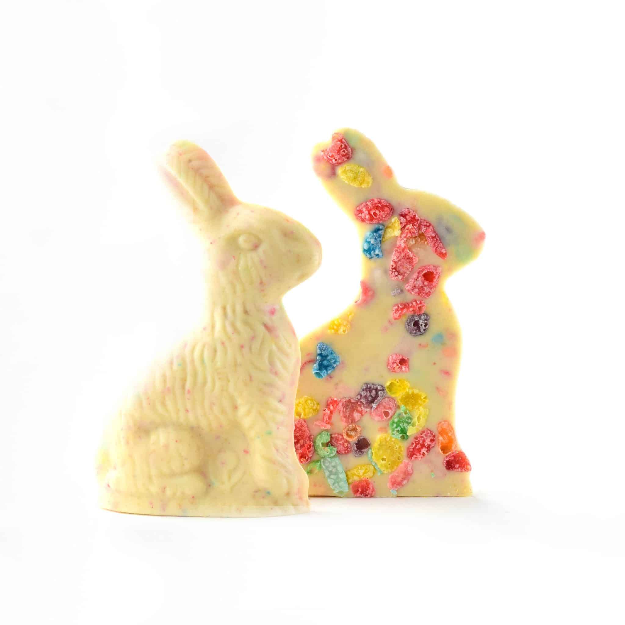 Two chocolate bunny figures on a white background, one plain and one decorated with colorful candy pieces.