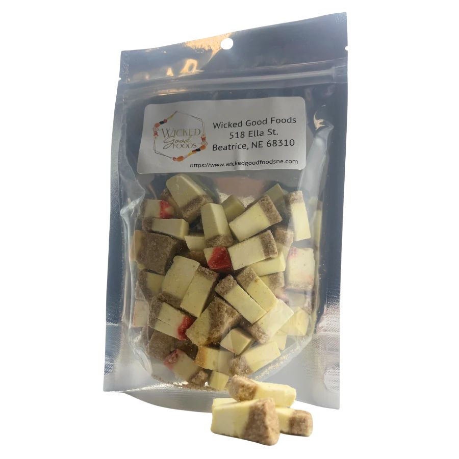 Another picture of freeze dried cheesecake bites on a white background with three cheesecake bites outside of the bag