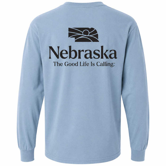 A light blue long-sleeve t-shirt shown from the back, featuring a black graphic of the Nebraska state silhouette with a sun and the text 'Nebraska The Good Life Is Calling.' printed on the back.