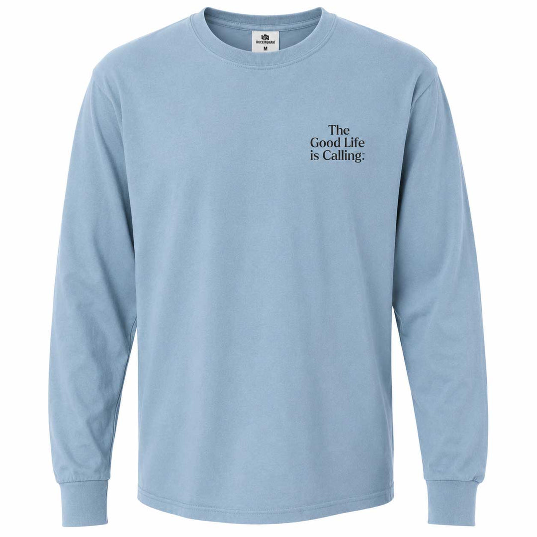 A light blue long-sleeve crewneck t-shirt with the text 'The Good Life is Calling.' printed in black serif font on the left chest, displayed on a clean white background.