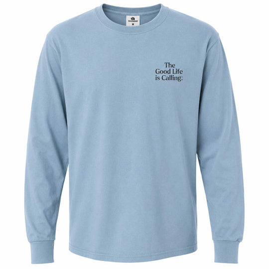 A light blue long-sleeve crewneck t-shirt with the text 'The Good Life is Calling.' printed in black serif font on the left chest, displayed on a clean white background.