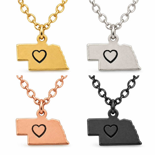 Four Nebraska-shaped pendant necklaces shaped like a state outline, shown in gold, silver, rose gold, and black finishes on matching chains against a white background.