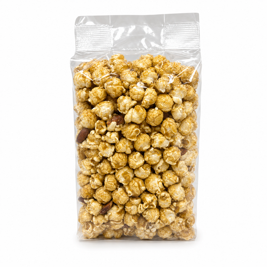A clear plastic resealable bag filled with caramel popcorn and a few dark chocolate pieces, photographed on a plain white background.