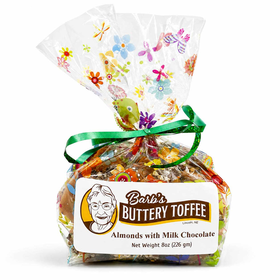 A 8 oz gift bag of Barb's Buttery Toffee Almonds with Milk Chocolate, wrapped in clear cellophane with a green ribbon and a floral pattern, on a white background.