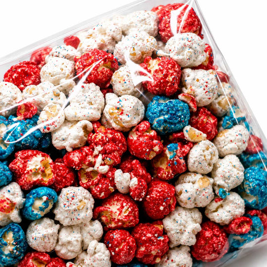 A clear plastic bag filled with coated popcorn in red, white, and blue, with multicolored sprinkles visible on the popcorn pieces.