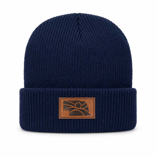 A navy blue ribbed knit beanie hat with a brown leather patch on the front cuff featuring a stylized mountain and sun logo.