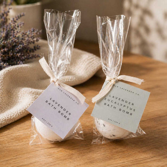 Two lavender bath bombs in clear packaging with labels on a wooden surface.